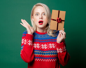 Wall Mural - Beautiful woman in Christmas sweater with gift box on green background