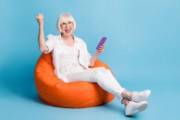 Canvas Print - Photo portrait of granny using smartphone gesturing like winner isolated on vibrant blue color background