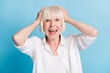 © deagreez - Photo portrait of amazed shocked grandmother keeping head with hands wearing white shirt isolated on vibrant blue color background