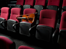 Violin Resting On Row Of Empty Red Auditorium Seats