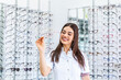 © Graphicroyalty - Attractive young female doctor in ophthalmology clinic. Doctor ophthalmologist is standing near shelves holding eyeglasses.