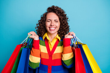 Canvas Print - Photo of beautiful dreamy young woman wear striped rainbow sweater raise shopping bags isolated on blue color background