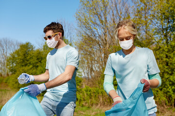 Canvas Print - volunteering, health and ecology concept - couple of volunteers wearing face protective medical masks for protection from virus disease with garbage bags cleaning area in park