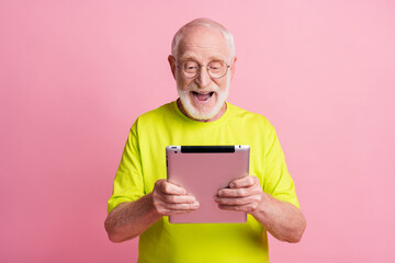 Wall Mural - Portrait of optimistic pensioner hold tablet wear spectacles green color t-shirt isolated on pastel pink color background