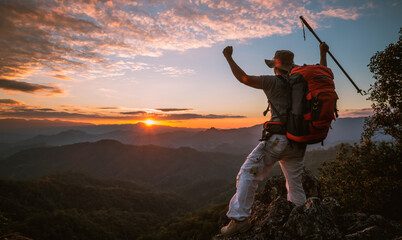 Wall Mural - young man hiker on a top of a mountain standing on top of cliff in summer mountains at sunset and en