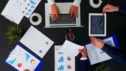 High angle view of business team working with financial reports at corporate office table analysing annual data planning next project. Manager sitting in conference room using modern technology.