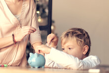 Mother And Child Putting Coin Into Piggy Bank. Education Of Children In Financial Literacy. Money, Cash, Investment.