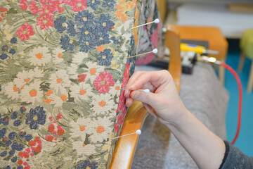 Woman hands sewing with upholstery round needle. Upholsterer working with fabric with flowers pattern. Hand sewing in upholstery workshop. 