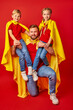 © Roman - caucasian man and kids in superhero cloaks, powerful father holds children on shoulders, look at camera