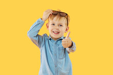 Portrait Of Surprised Cute Little Child Boy In Sunglasses. Child Having Fun Isolated Over Yellow Background. Looking At Camera. Showing Thumbs Up Sign Ok. Wow Funny Face.