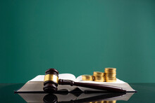 Stack Of Coins With Gavel Over Open Book On Table Against Green Background