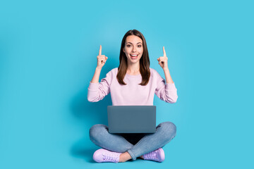 Full size photo of positive girl sit floor legs crossed work remote laptop demonstrate social network promo wear lilac violet pullover denim jeans isolated over blue color background