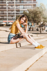 Wall Mural - Long board girl sitting on the stairs outdoors with a skateboard in summer. Sunny day for outside activities. Cool California concept