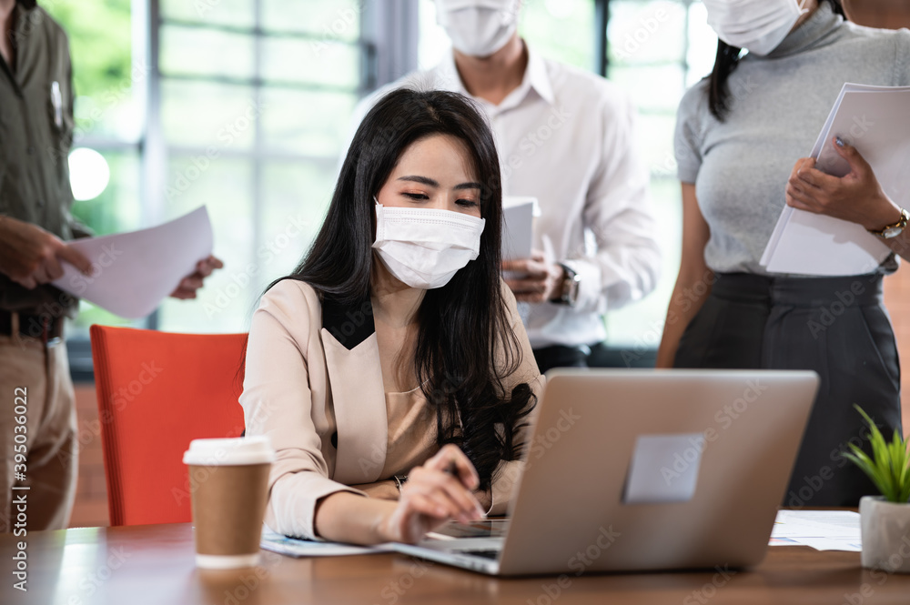 Attractive Asian female boss supervisor wear protective face mask in New normal office teaching and explaining intern or new employee to use corporate software or helping with difficult assignment - obrazy, fototapety, plakaty 