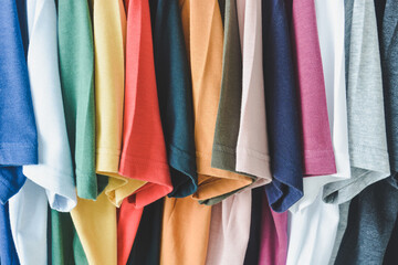 close up collection of colorful t-shirts hanging on clothes hanger in closet or clothing rack