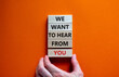 Wooden blocks with words 'we want to hear from you'. Male hand. Beautiful orange background. Copy space. Business and support concept.