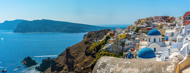 Wall Mural - A panorama view of the village of Oia, Santorini and the island of Thirasia in the background in summertime