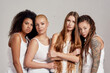 © Svitlana - Portrait of four young diverse women, female friends wearing white shirts looking at camera while posing together isolated over grey background