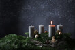 First advent with one burning candle on fir branches with Christmas decoration against a dark grey background, copy space