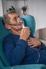 elderly senior sits in a armchair with an oxygen mask in quarantine at home