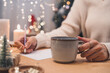 © Anna - Goals plans make to do and wish list for new year christmas concept writing in notebook. Woman hand holding pen on notepad and coffee cup at home on winter holidays xmas.