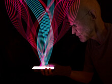 Man Holding Illuminated Mobile Phone With Light Trails Against Black Background