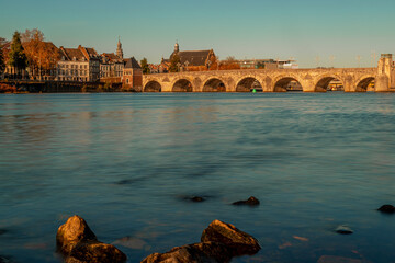 Low angle view over the water with the historical skyline of Maastricht with the old bridge connecting two parts of town crossing the river Meuse. 