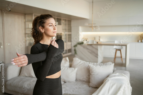workout fitness aerobics gymnastics at home in the living room, comfortable sportswear in black. A woman is engaged in her health doing stretching and cardio exercises. Large bright apartment.