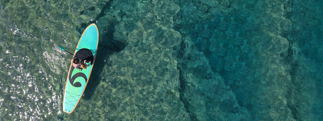 Wall Mural - Aerial drone ultra wide top down photo of fit unidentified woman paddling on a SUP board or Stand Up Paddle in Mediterranean turquoise clear sea