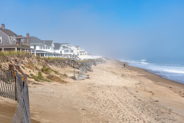 Person strolling along a sandy beach lined with holiday homes on a misty autumn morning, Seabrook, NH, USA.