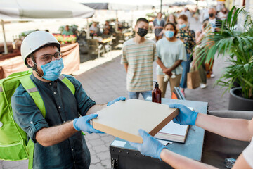 Wall Mural - Delivery man wearing mask and protective gloves receiving pizza while collecting orders from the pickup point during coronavirus lockdown