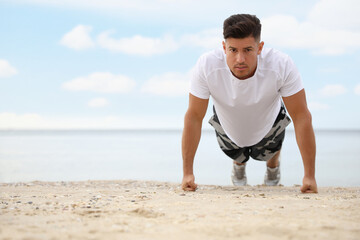 Canvas Print - Muscular man doing push up on beach, space for text. Body training