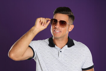 Wall Mural - Handsome man wearing sunglasses on purple background