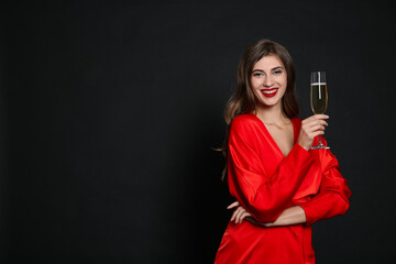 Happy woman with glass of champagne on black background, space for text. Christmas party