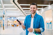 © wpadington - Attractive young casually dressed bearded man smiling and posing in the mall with mobile phone and a bunch of shopping bags in hands