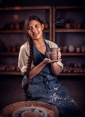 Wall Mural - Young and cheerful woman admires the work done in the pottery workshop. Making ceramic dishes.