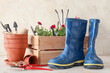 Gardening tools with gumboots and pot flowers on light background