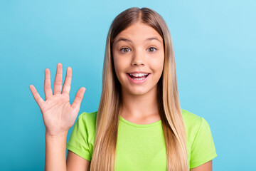 Wall Mural - Portrait of young happy positive good mood smiling girl holding hand say hello wear green t-shirt isolated on blue color background