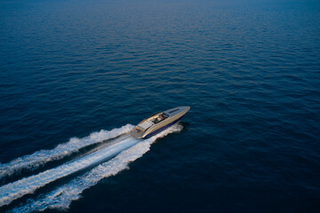 Large speed boat moving at high speed side view. Drone view of a boat  the blue clear waters at sunset. The boat is gray-blue combined color. Top view of a boat sailing to the blue sea.