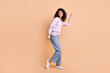 Full size profile photo of optimistic curly girl dancing wear sweater jeans sneakers isolated on peach color background