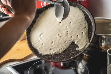 Person pouring the dough into a hot pan and frying homemade pancakes. Concept of making pancakes in your own kitchen