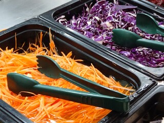 salad bar show fresh red cabbage and fresh orange carrot fine slice in black square shape container with black plastic 2 Food tongs