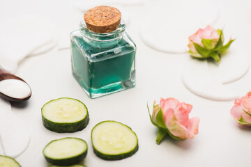 Wall Mural - cucumber slices near corked bottle of homemade lotion, tea roses, and cotton pads on white blurred 