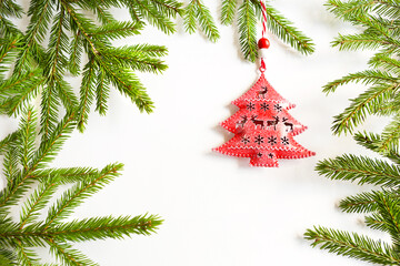 Red toy in the shape of a Christmas tree on the green branches of a natural spruce on a white background, frame. Copy space. Christmas, new year. Decor with slits in the shape of deer, snowflakes.