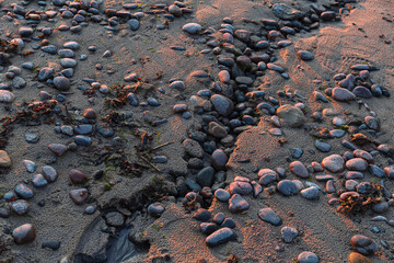 Pebble beach close-up with surfing sea in a sunset light. Stones of different sizes on the background of the sea in evening sunset.