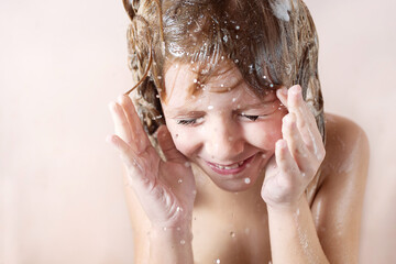 Wall Mural - charming little blonde girl washes her hair in the bathroom with foam on her head. water pours, drop