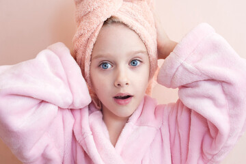 Wall Mural - a little girl with blue eyes in a pink robe and a pink towel on her head after a bath smiles and loo