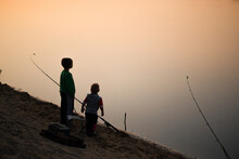Children Fishermen On The River Bank At Sunset