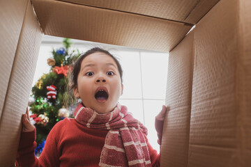 Wall Mural - merry christmas and happy holidays. cheerful cute child girl opening a christmas present. little kid having fun near christmas tree indoors. view from inside of the box.