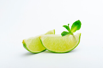 Two lime wedges and green mint leaves on the white background.Ingredients for preparing food and drinks